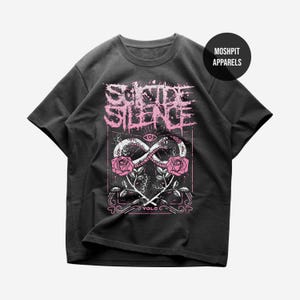 Könnte beinhalten: Dunkelgraues T-Shirt mit einem rosa und weißen Grafikdesign. Das Design enthält den Text "SUICIDE SILENCE", ein Unendlichkeitssymbol mit einer Schlange, Rosen und den Text "VOLC". Das T-Shirt hat kurze Ärmel und einen Rundhalsausschnitt.