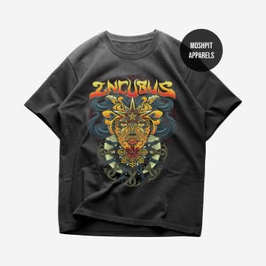 May include: Dark grey t-shirt with a vibrant graphic of a face with a star-shaped headpiece and the word "INCUBUS" in orange and yellow. The design incorporates blue, orange, and yellow colours. The shirt has a crew neck and short sleeves. The brand name "MOSHPIT APPARELS" is in a black circle.