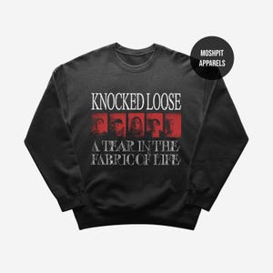 Puede incluir: Sudadera gris oscuro con el texto "KNOCKED LOOSE" encima de "A TEAR IN THE FABRIC OF LIFE" en blanco. El diseño incluye rectángulos rojos con imágenes de personas. Un círculo negro con "MOSHPIT APPARELS" está en la parte superior derecha.