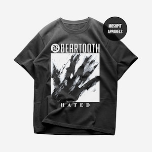 May include: Dark grey t-shirt with the band name "BEARTOOTH" in white above a black and white abstract design. The word "HATED" is printed in white below the design. A round logo with "MOSHPIT APPARELS" is on the upper right.