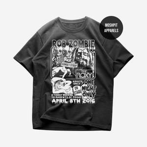 May include: Black t-shirt featuring a graphic promoting a Rob Zombie concert at The Roxy on Sunset Strip. The design includes the text "Rob Zombie," "Riot on Sunset Strip," and "April 8th 2016." The shirt also has the text "Moshpit Apparels."