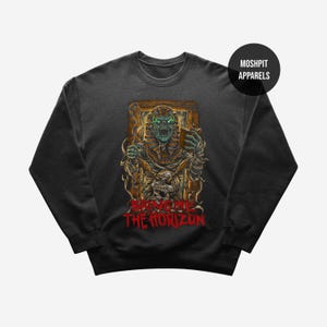 May include: Dark gray sweatshirt featuring a graphic of a mummy holding a drink, with glowing green eyes. The design includes a skull and the text "BRING ME THE HORIZON" in red. The sweatshirt has a crew neck and long sleeves.