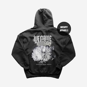 Może przedstawiać: Ciemnoszara bluza z kapturem z dużą grafiką na plecach. Grafika zawiera tekst "WE CAME AS ROMANS" w stylizowanej czcionce nad biało-szarym wzorem drzewa. Tekst "TRACING BACK ROOTS" znajduje się pod drzewem.