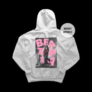 May include: A pale grey hoodie with a graphic on the back. The graphic shows a woman playing a guitar, with the words "BEAT TOP" in pink. The brand name "MOSHPIT APPARELS" is printed on the upper right.