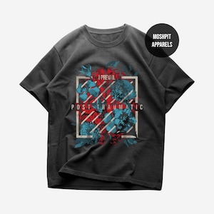May include: Dark gray t-shirt featuring a floral design with red and blue flowers inside a white rectangular frame. The text "I PREVAIL" is above the frame, and "POST TRAUMATIC" is below. A black circle with "MOSHPIT APPARELS" is in the upper right.