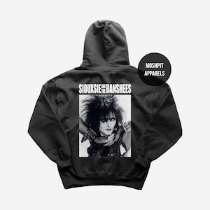 Può includere: Felpa con cappuccio nera con un'immagine in bianco e nero di Siouxsie Sioux e la scritta "Siouxsie and the Banshees". La felpa con cappuccio presenta anche la scritta "Moshpit Apparels" in un design circolare.