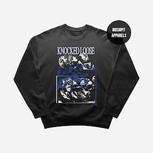 Puede incluir: Sudadera negra de cuello redondo con el texto "KNOCKED LOOSE" en azul. El diseño incluye un gráfico azul y blanco con el texto "A DIFFERENT SHADE OF BLUE". Un círculo negro con "MOSHPIT APPARELS" está en la parte superior derecha.