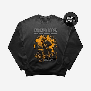 Puede incluir: Sudadera gris oscuro con cuello redondo con el texto "KNOCKED LOOSE" en blanco, sobre un gráfico amarillo y negro. El gráfico incluye el texto "justice for the damned + reactions" y "RAD BAR, WOLLONGONG". Un círculo negro con "MOSHPIT APPARELS" está en la parte superior derecha.