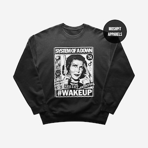 Könnte beinhalten: Schwarzes Sweatshirt mit Rundhalsausschnitt und Grafikdruck. Der Druck zeigt den Text "SYSTEM OF A DOWN", eine Frau mit einer Pistole und die Worte "RESIST suffering" und "#WAKEUP". Das Logo "MOSHPIT APPARELS" befindet sich oben rechts.