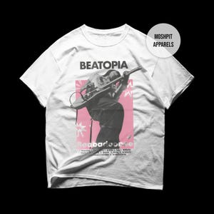 May include: White t-shirt with a graphic of a musician playing a guitar, set against a pink backdrop. The shirt has the word "BEATOPIA" above the graphic and "Readbadcorcee" below. The brand name "MOSHPIT APPARELS" is on the upper right.
