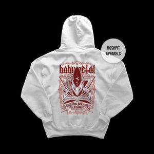 May include: White hooded sweatshirt with a red graphic on the back. The graphic features the text "baby metal" above a stylized illustration of a creature with a book and the text "for god know..." below. The brand name "Moshpit Apparels" is on the right.