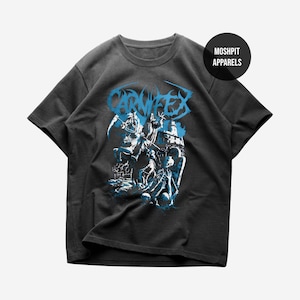 Puede incluir: Camiseta gris oscuro con un gráfico azul que representa una escena de batalla y la palabra "CARNIFEX". La camiseta tiene cuello redondo y mangas cortas. El nombre de la marca "MOSHPIT APPARELS" está impreso en un círculo negro.