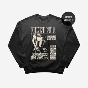 Może przedstawiać: Ciemnoszara bluza z czarno-białą grafiką. Grafika zawiera tekst "BIKINI KILL", "MOLLY MCGUIRE", "REVOLUTION GIRL STYLE NOW" i "FRI SEPT 25TH OUT HOUSE". Logo "MOSHPIT APPARELS" znajduje się w prawym górnym rogu.