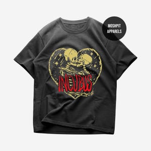 May include: Black t-shirt with a heart-shaped design featuring two skulls and the word "INCUBUS" in red. The design is in yellow and is surrounded by stars. The shirt has a crew neck and short sleeves. The brand name "MOSHPIT APPARELS" is printed on a black circle.