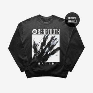May include: Black crew neck sweatshirt featuring the band name "BEARTOOTH" in white above a black and white abstract design. The word "HATED" is printed in white below the design. A black circle with "MOSHPIT APPARELS" is in the upper right corner.