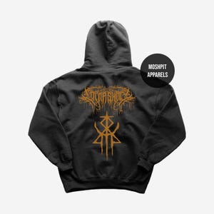 May include: Dark gray hoodie with a hood and long sleeves. The back features a gold-colored graphic design with the text "VOTNA SHOT" and a stylized symbol. A black circle with "MOSHPIT APPARELS" is on the right.