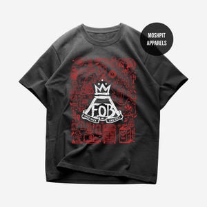 Pode incluir: T-shirt cinzenta escura com um design gráfico vermelho e branco. O design inclui uma coroa, as letras "FOB" e o texto "Save Rock and Roll". A camisa também apresenta várias ilustrações.