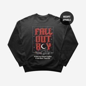 May include: Dark grey sweatshirt with a graphic featuring the text "FALL OUT BOY" in red, with a car illustration and the text "A Little Less Sixteen Candles, A Little More 'Touch Me'". The sweatshirt has a crew neck.