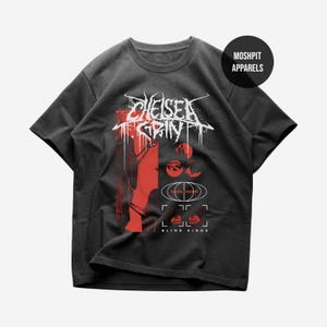 Puede incluir: Camiseta gris oscuro con un diseño gráfico rojo y blanco. El diseño incluye el texto "Chelsea Grin" en una fuente estilizada, junto con otros elementos gráficos y el texto "Blind Kings". La camiseta tiene mangas cortas y cuello redondo.