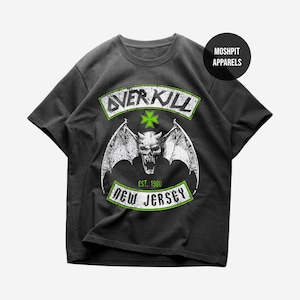 May include: Dark gray t-shirt with a distressed graphic featuring a skull with bat wings, the word "OVERKILL", a cross, and "NEW JERSEY EST. 1980". The shirt has a round neckline and short sleeves. The brand name "MOSHPIT APPARELS" is printed on a black circle.