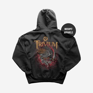May include: Dark gray hoodie featuring the band name "Trivium" in gold lettering, with a graphic of a skeletal figure and a red and orange design. The hoodie has a hood and the text "Moshpit Apparels" on the upper right.