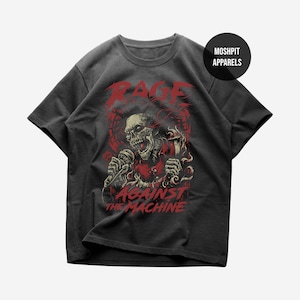 Puede incluir: Camiseta gris oscuro con un gráfico rojo de una calavera sosteniendo un micrófono, con las palabras "RAGE" arriba y "AGAINST THE MACHINE" abajo. La camiseta tiene cuello redondo y mangas cortas. El nombre de la marca "MOSHPIT APPARELS" está impreso en un círculo negro.