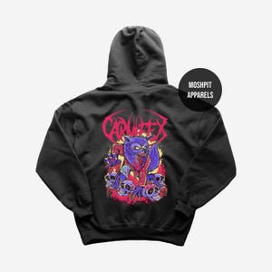May include: Black hoodie featuring a purple werewolf graphic with skulls and the word "CARNIFEX" in red. The brand name "MOSHPIT APPARELS" is printed on a black circle. The design is on the back of the sweatshirt.