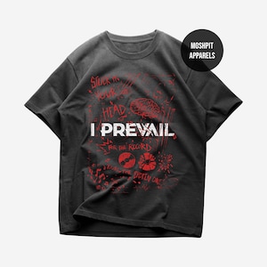 Puede incluir: Camiseta gris oscuro con un diseño gráfico rojo. El diseño incluye las palabras "I Prevail", "Stuck in Your Head" y otros textos e ilustraciones. Un círculo negro con "Moshpit Apparels" está en la parte superior derecha.