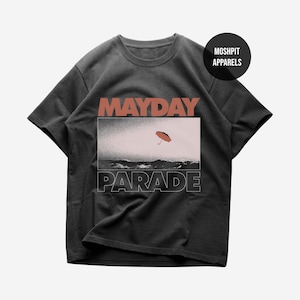 May include: Dark gray t-shirt featuring the words "MAYDAY PARADE" in a bold, stylized font. The shirt's graphic includes a scene with an orange umbrella over a body of water. The shirt is from Moshpit Apparels.