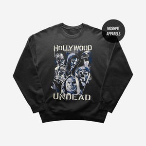 May include: Dark gray sweatshirt featuring a graphic of masked figures with the text "HOLLYWOOD UNDEAD" in white and blue. The design includes various mask styles and the brand name "Moshpit Apparels".