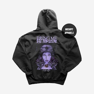 May include: Dark gray hoodie with a graphic featuring a woman wearing a lion headdress, a triangle with an eye, and the text "BRING ME THE HORIZON". The hoodie has a drawstring hood and a kangaroo pocket. The brand name "MOSHPIT APPARELS" is on the right side.