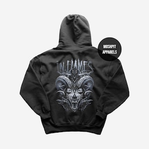 May include: Dark gray hoodie featuring a detailed illustration of a wolf with ram horns and the text "IN FLAMES" in a stylized font. The design is centered on the back of the hoodie, with a "MOSHPIT APPARELS" logo on the upper right.