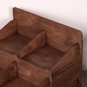 Op de afbeelding: Een donkerbruine houten bureau-organizer met meerdere compartimenten, schuine zijpanelen en een hoge achterwand. De structuur is opgebouwd uit platte houten onderdelen die samen een open opbergeenheid vormen met een zichtbare houtnerf.