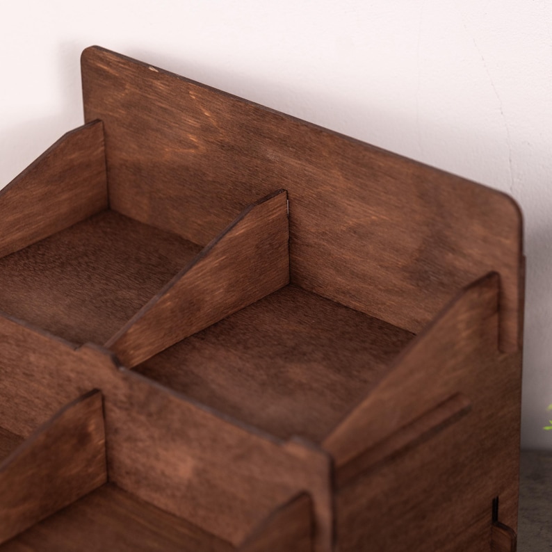 Op de afbeelding: Een donkerbruine houten bureau-organizer met meerdere compartimenten, schuine zijpanelen en een hoge achterwand. De structuur is opgebouwd uit platte houten onderdelen die samen een open opbergeenheid vormen met een zichtbare houtnerf.