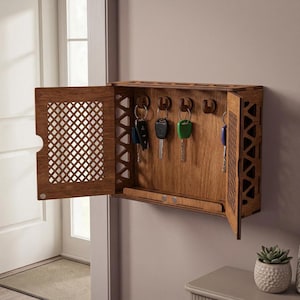 Peut inclure: Un porte-clés en bois avec une porte ouverte, révélant plusieurs clés suspendues à l'intérieur. Le porte-clés est monté sur un mur de couleur claire. La porte présente un motif en treillis décoratif. Le porte-clés est en bois.