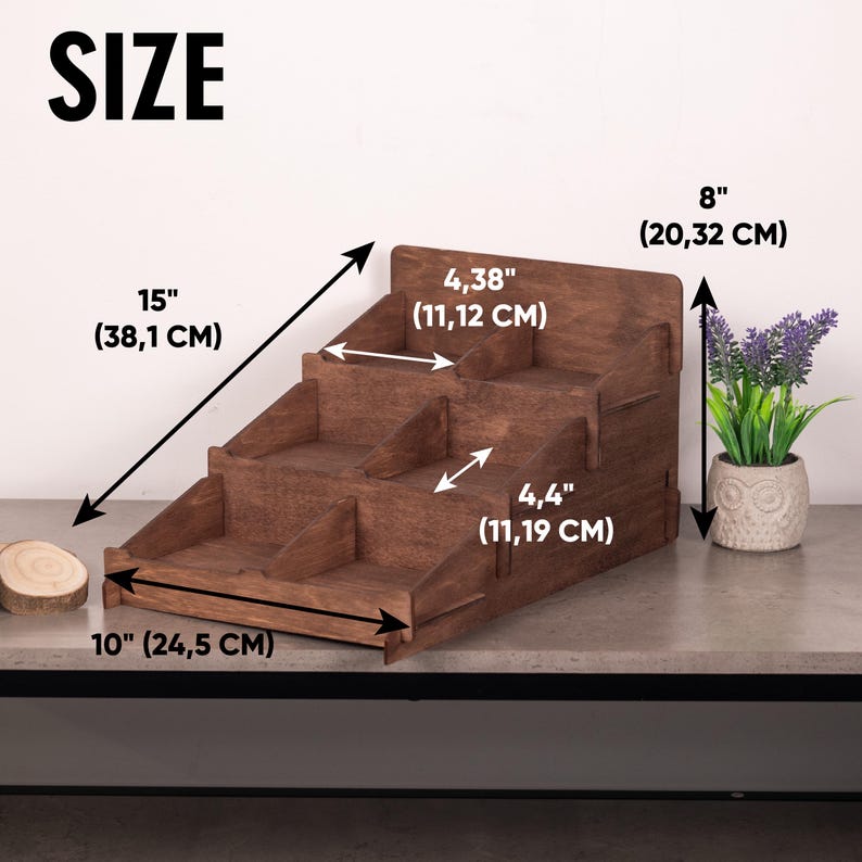 Op de afbeelding: Een donkerbruine houten displaystandaard met drie niveaus en verdelers. De afmetingen zijn aangegeven als 38,1 cm diep, 24,5 cm breed, 20,32 cm hoog, met schapdieptes van 11,12 cm en 11,19 cm. De standaard heeft een getrapt ontwerp.
