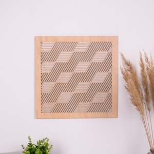 Op de afbeelding: Vierkante houten wandkunst met een geometrisch patroon. Het kunstwerk heeft een herhalend ontwerp van schuine lijnen en vormen, waardoor een driedimensionaal effect ontstaat. Het frame en het ontwerp zijn in natuurlijke houttinten.