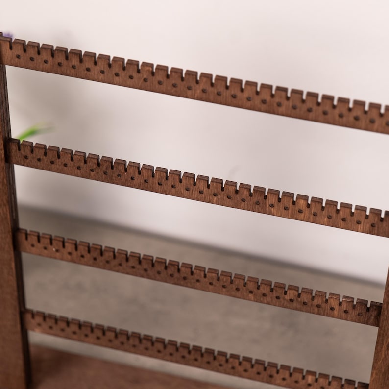 Puede incluir: Un expositor de pendientes de madera de color marr&oacute;n oscuro con cuatro barras horizontales. Cada barra tiene una serie de peque&ntilde;os orificios espaciados uniformemente a lo largo del borde superior, dise&ntilde;ados para sostener varios pares de pendientes.