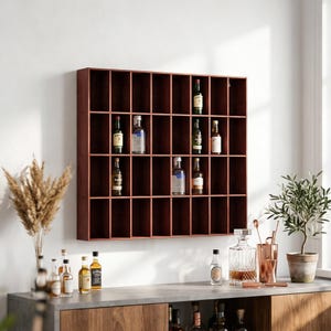 Pode incluir: Um armário de licor de madeira vermelho escuro montado na parede com vários compartimentos, exibindo várias garrafas de licor. O armário é retangular e tem uma estrutura em grade. Uma área de bar com garrafas e utensílios de bar em primeiro plano.