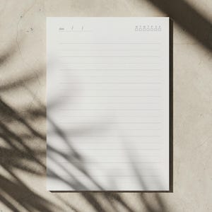 Pode incluir: Uma folha de bloco de notas retangular branca com linhas horizontais para escrever, um campo de data no canto superior esquerdo e uma linha de sete pequenas caixas marcadas com as letras M, T, W, T, F, S, S para os dias da semana.