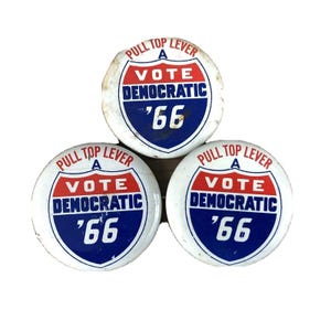 Könnte beinhalten: Drei Vintage-Wahlkampfknöpfe. Jeder Knopf ist rund mit weißem Hintergrund und einem rot-weiß-blauen Design. Der Text auf den Knöpfen lautet "PULL TOP LEVER", "VOTE DEMOCRATIC" und "'66".