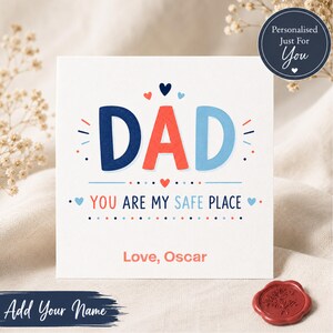 May include: A square greeting card with the word "DAD" in blue and red letters. The text "YOU ARE MY SAFE PLACE" is below. The card includes the text "Love, Oscar" and a circular sticker that says "Personalised Just For You".