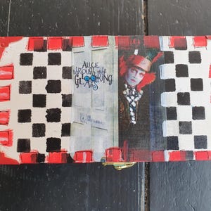 Peut inclure: Une boîte rectangulaire en bois avec un motif à damier noir et blanc sur les côtés, des bords peints en rouge et un graphique central représentant le Chapelier Fou avec le texte Alice Through the Looking Glass et un loquet en laiton.