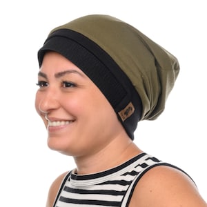 Könnte beinhalten: Olivgrüne und schwarze Beanie-Mütze. Die Mütze hat ein schwarzes Rippenband und eine weiche, drapierte Krone. Ein kleines braunes Lederetikett mit Logo ist an der Seite angenäht. Die Person im Bild trägt ein schwarz-weiß gestreiftes Tanktop.