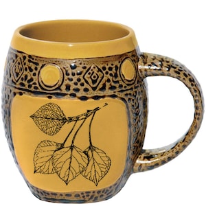 May include: A barrel-shaped ceramic mug featuring a smooth mustard yellow rim and a central panel displaying a black line drawing of three leaves on a branch. The exterior has a textured brown speckled finish with embossed geometric patterns.