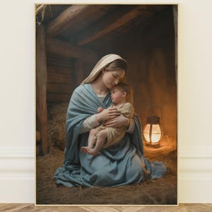 May include: A framed print depicts a tender scene of a mother cradling a child. The mother is draped in a blue robe and veil, while the child is wrapped in a cream-colored cloth. A lantern casts a warm glow in the background, illuminating a rustic wooden structure.