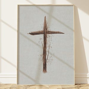 May include: A framed print featuring a rustic cross design. The cross is rendered in shades of brown, with a textured appearance against a light gray background. The artwork is displayed in a room with natural light and wooden flooring.