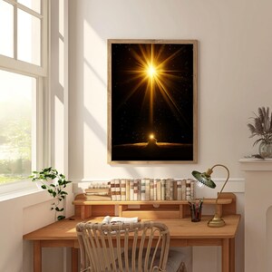 May include: A framed art print featuring a bright golden light emanating from a dark background. The artwork is displayed above a wooden desk with books, a lamp, and a woven chair. The room has a window with natural light.