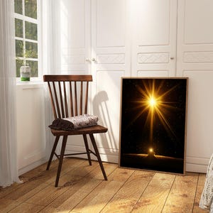 May include: A framed art print featuring a bright golden starburst against a black background. The artwork is displayed in a room with a wooden chair and a window with natural light.