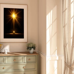 May include: A framed art print featuring a bright, golden starburst against a dark background. The artwork is displayed above a light green dresser with wooden knobs. A glass bowl of lemons and a small plant in a white pot are also visible.